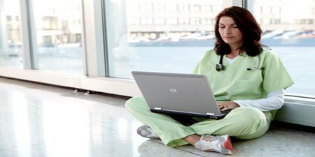 Arzt sitzt auf dem Boden und liest auf seinem Laptop
